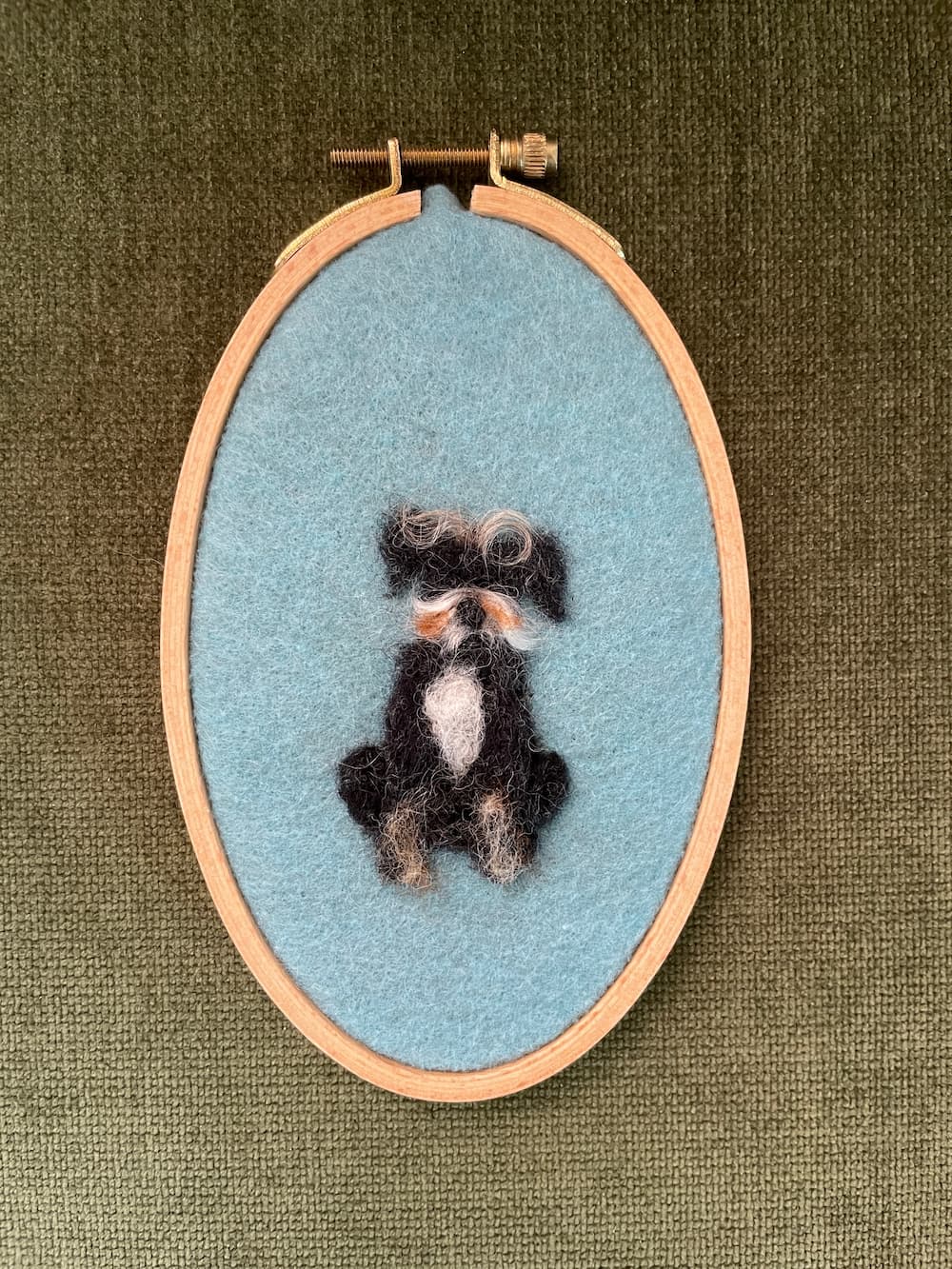 A needle felted portrait of a scruffy black dog named Jolene on a blue background.