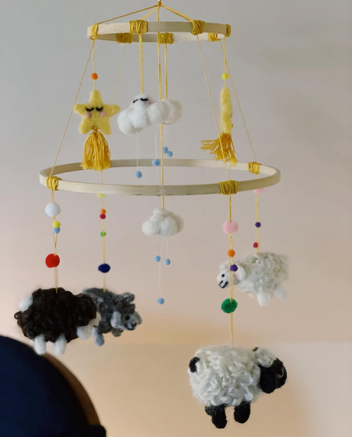 A needle felted mobile for a baby's nursery with shooting stars, clouds, and sheep hanging from it.